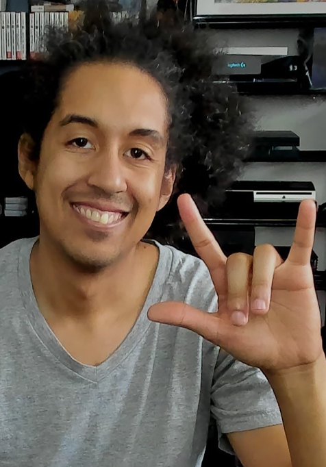DeafGamersTV smiles at the camera and uses his right hand to show the American Sign Language sign for I Love You.
