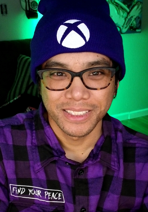 MikeTheQuad smiles at the camera, wearing a purple plaid shirt and a purple beanie with a white Xbox logo.